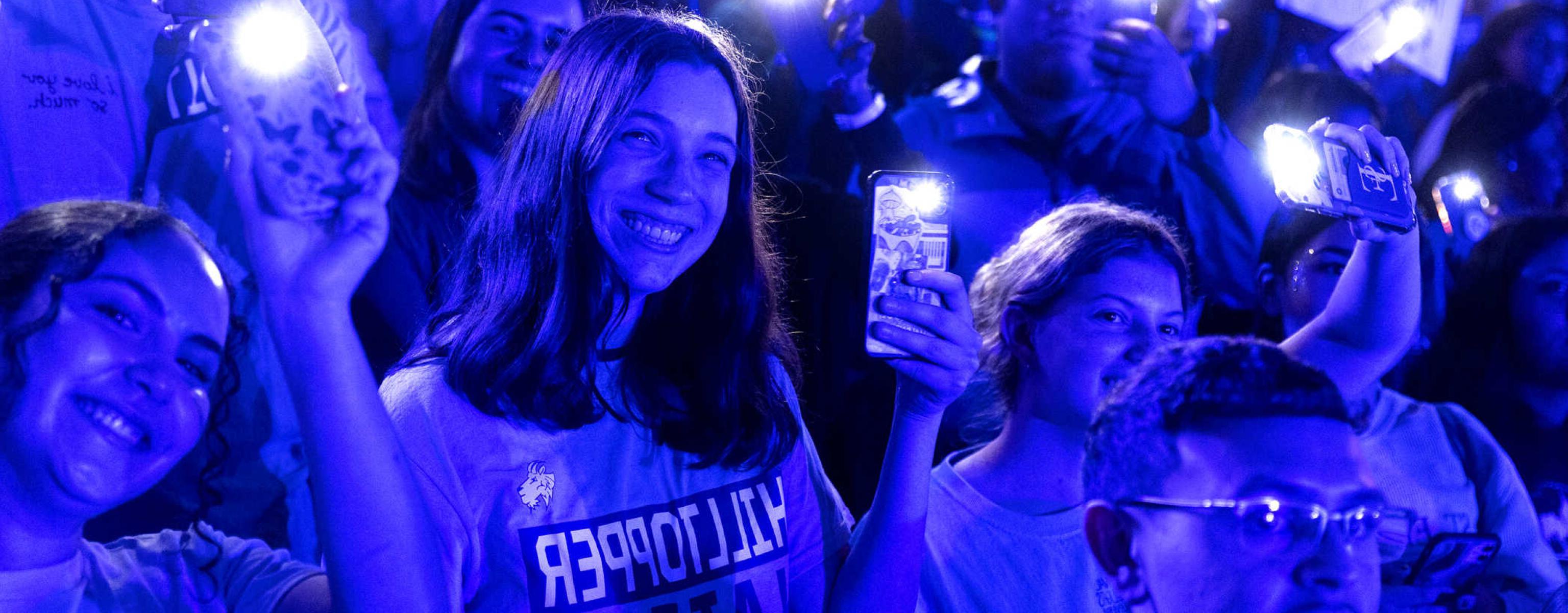 Students are illuminated by blue light and their cell phone flashlights during a pep rally.